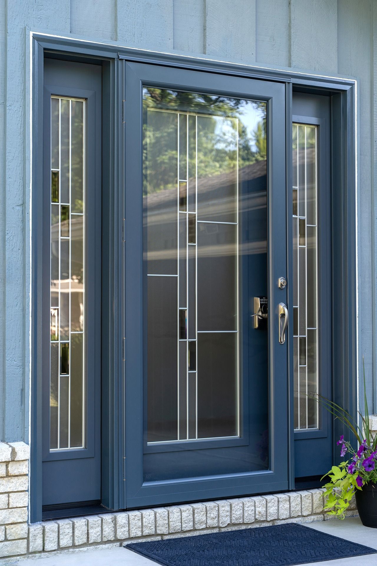 Blue front door with side windows, brick base, and welcome mat.