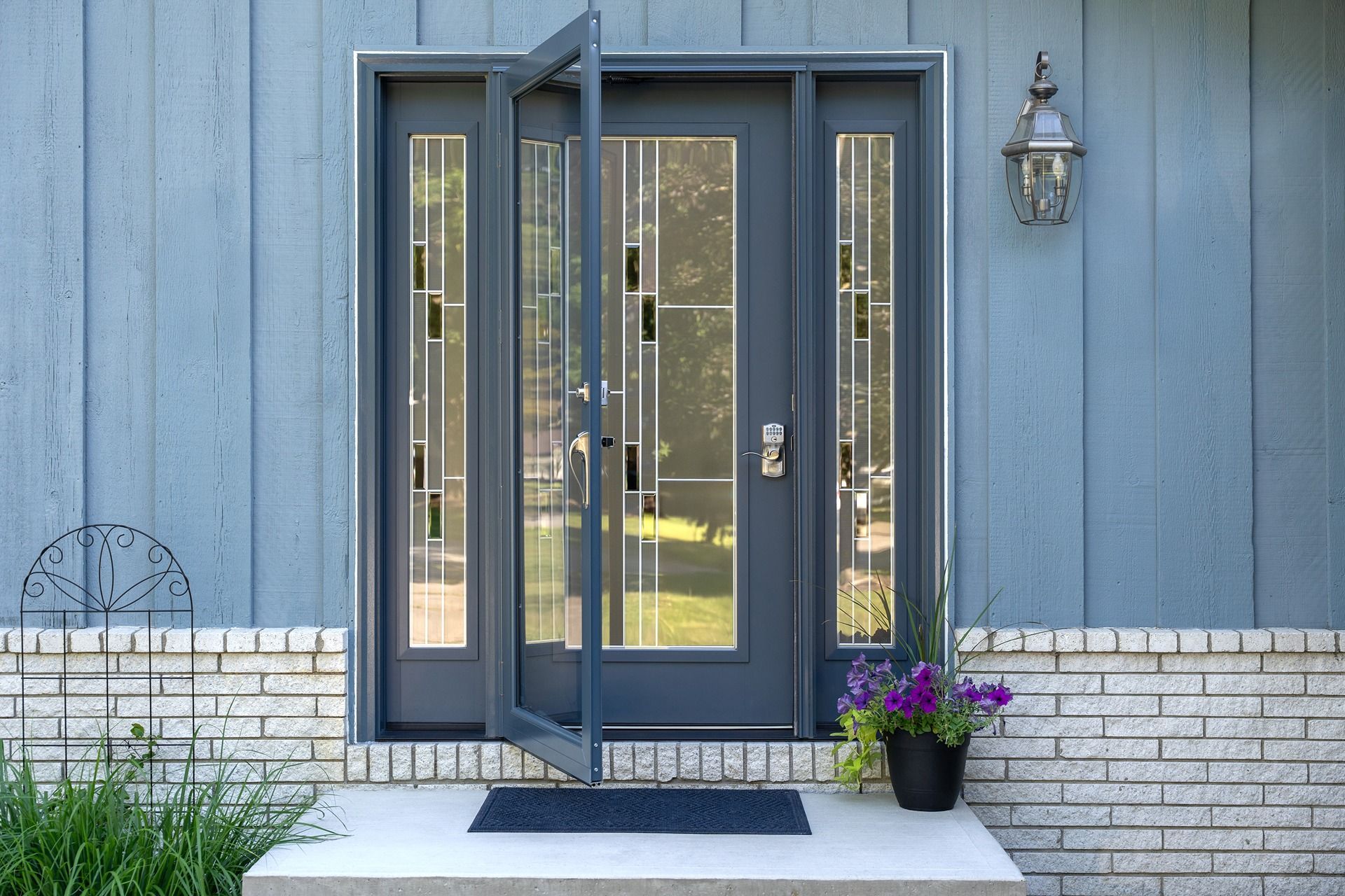 Blue front door with sidelights, one door open, on a white brick porch.