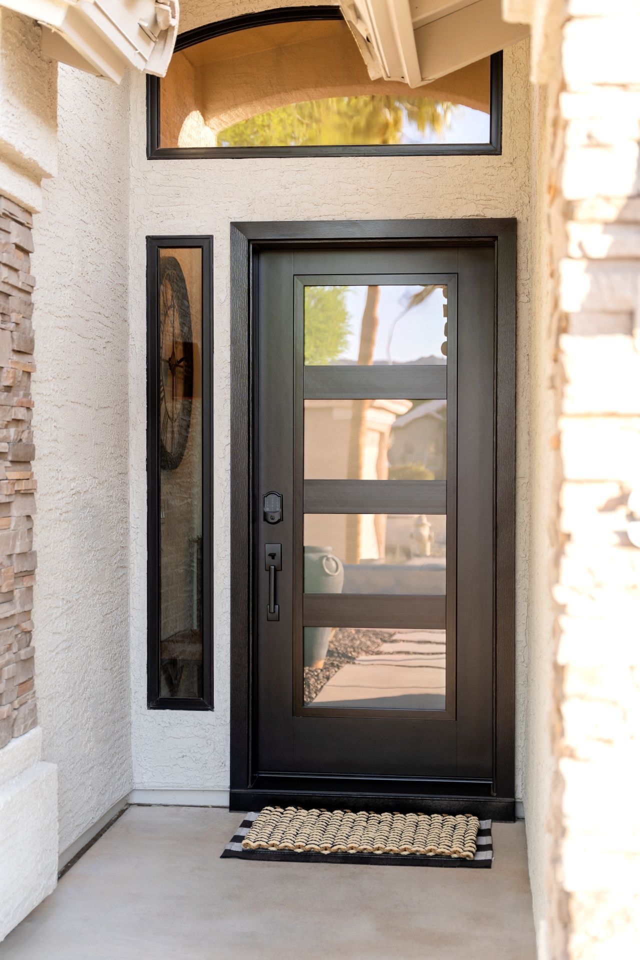Black front door with glass panels and sidelight, tan stucco exterior.