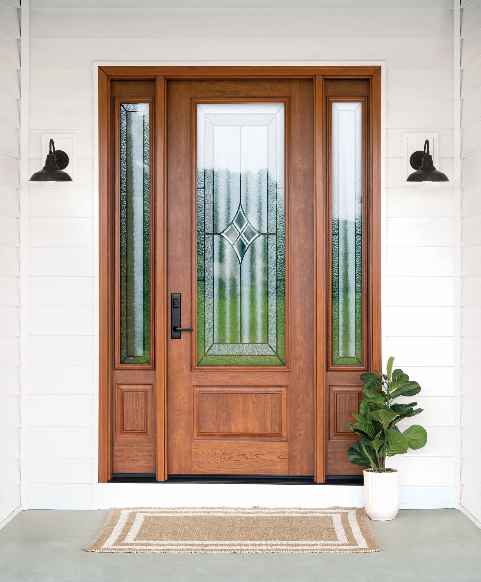 Wooden front door with glass panels, sidelights, and a small potted plant on a porch.