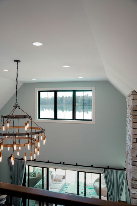 High-ceilinged room with chandelier and window overlooking water. Pale blue walls, dark window frame.