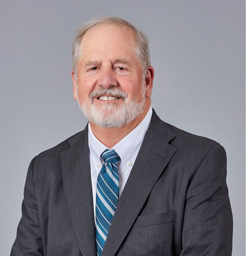 Man with gray beard, smiling, wearing a blue suit and tie.