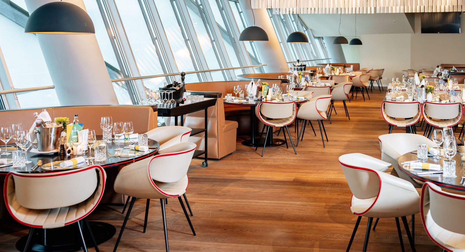 Modernes Restaurant mit weißen Stühlen, runden Tischen, Holzböden und großen Bogenfenstern mit Blick auf das Wasser