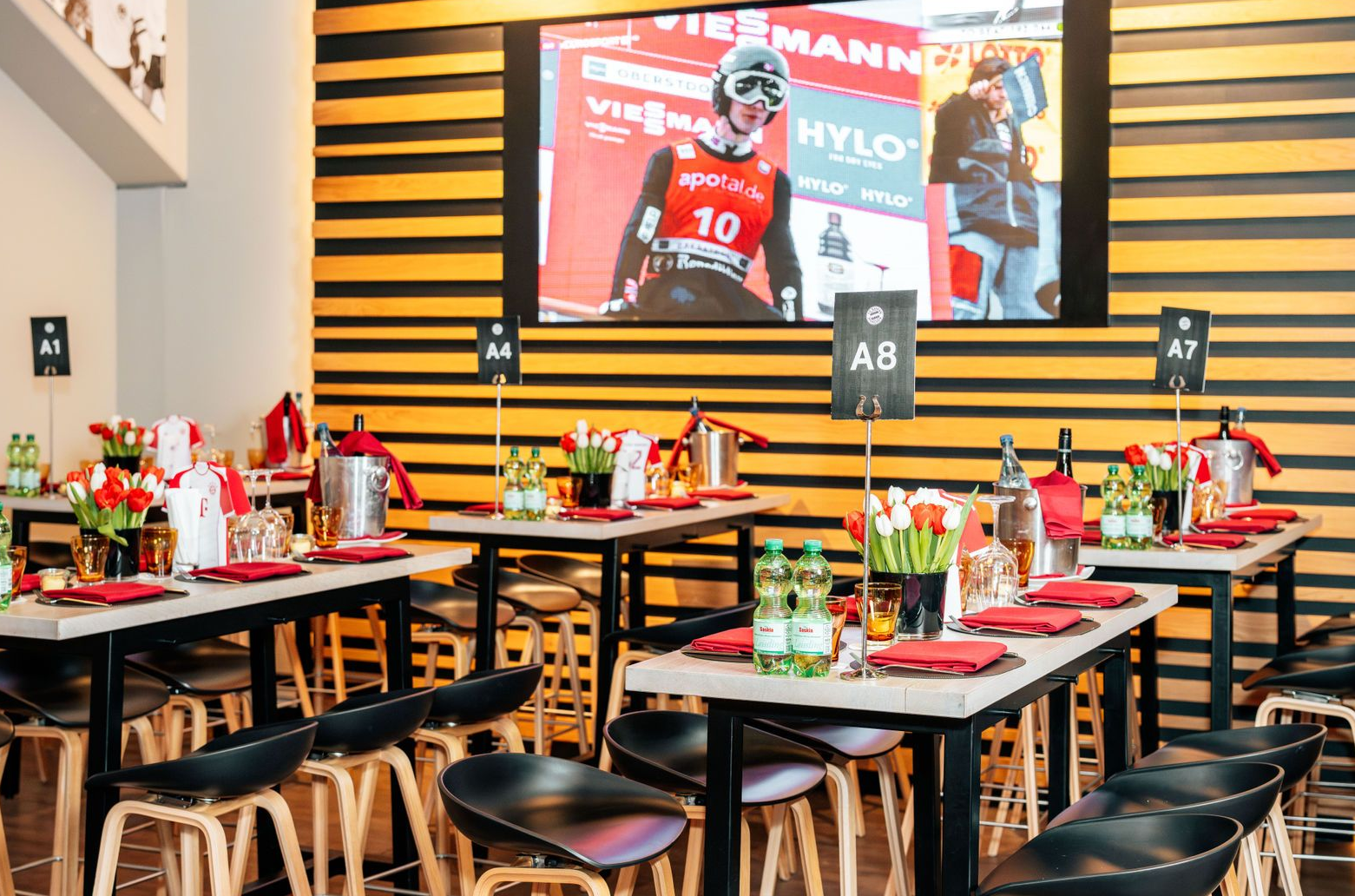 Essbereich einer Sportsbar mit Tischen, rotem Gedeck und einem großen Fußball-Wandbild an der Wand.