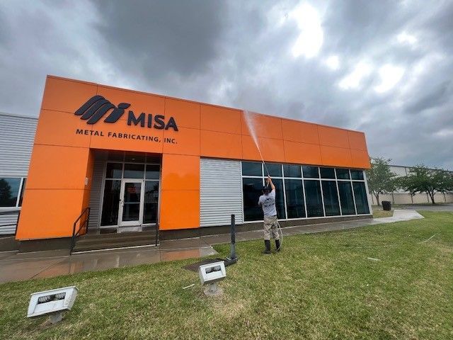 Person power washing an orange and white MISA Metal Fabricating Inc. building exterior.