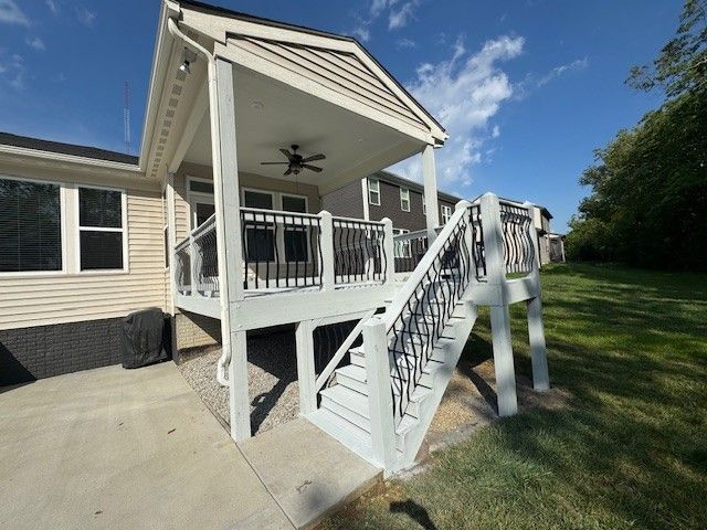 Deck with stairs and covered patio attached to a house with black railing, light color.