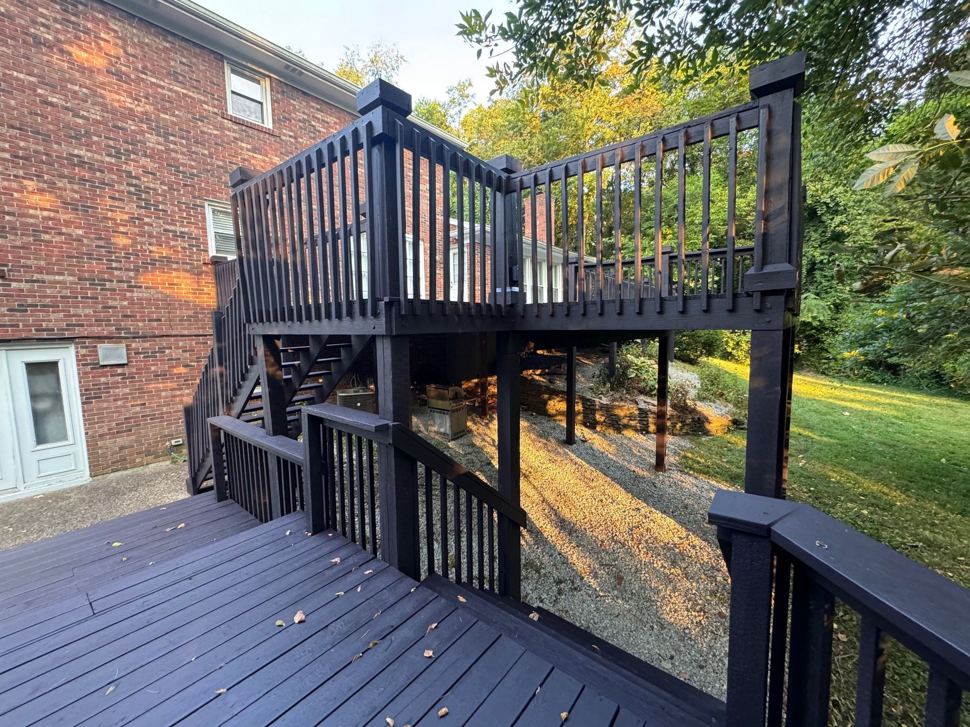 A black deck with stairs leading up to it is in front of a brick house. - Bourbon City Softwash - Louisville, KY