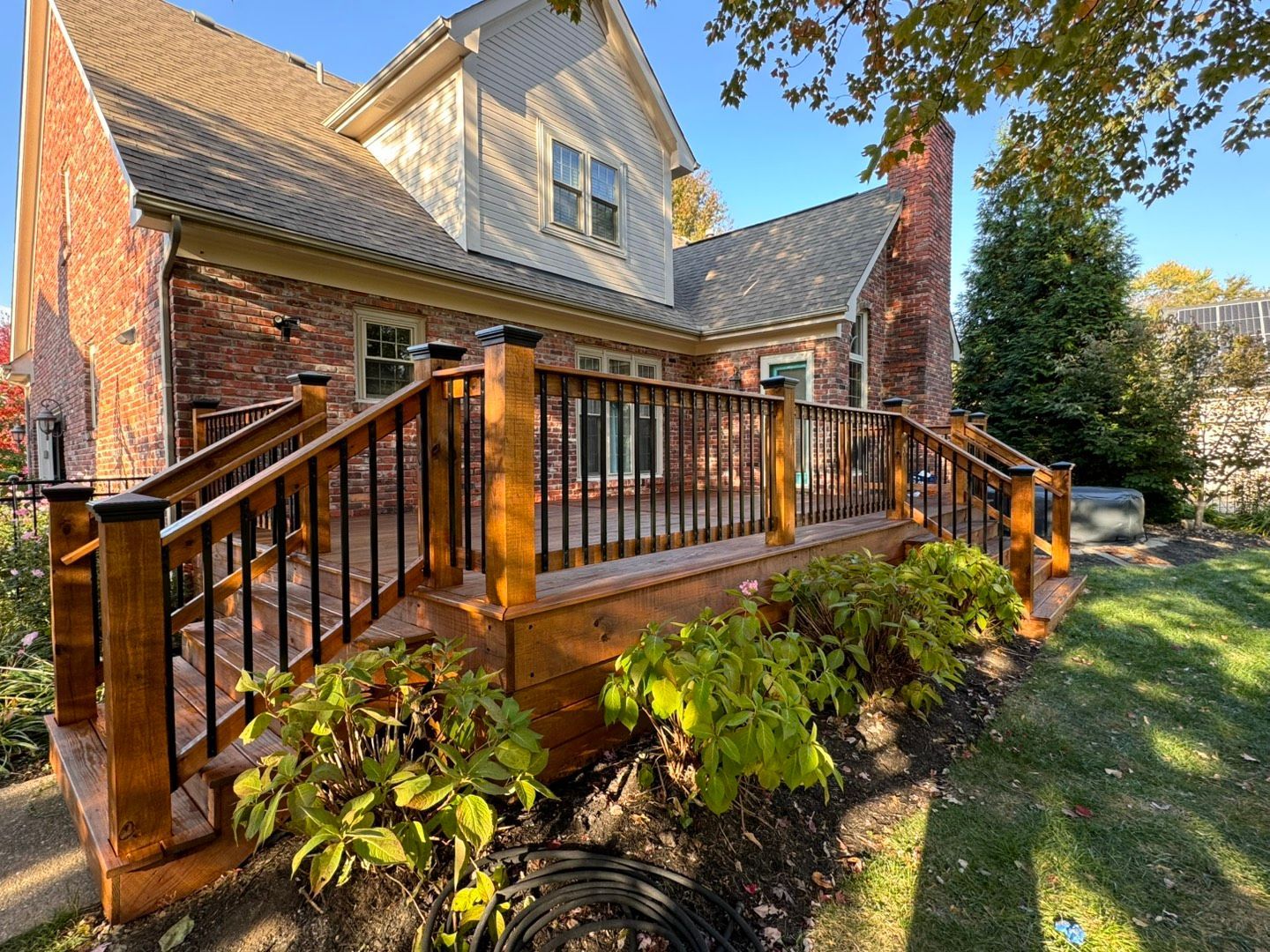 Wooden deck attached to a red brick house with black railings and lush greenery.