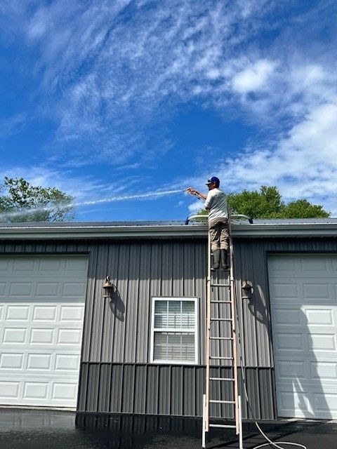 A man is standing on a ladder washing the roof of a building. - Bourbon City Softwash - Louisville, KY