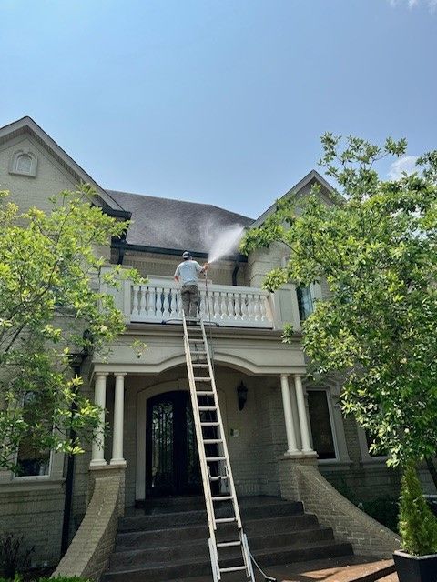 A man on a ladder is cleaning the roof of a house. - Bourbon City Softwash - Louisville, KY