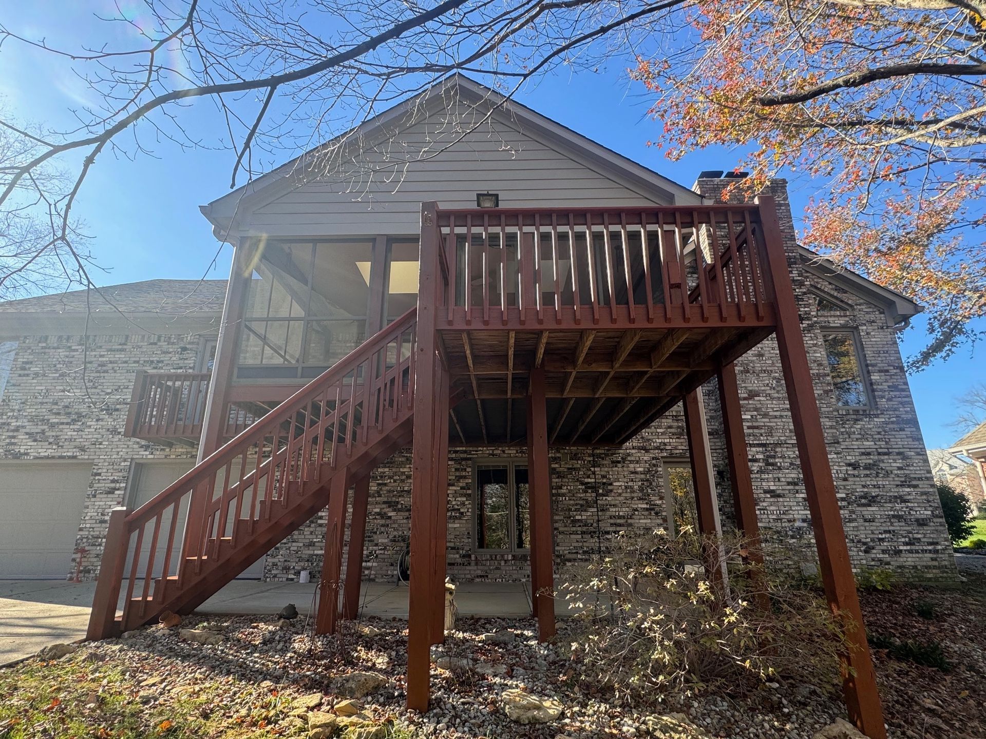 Two-story house with a wooden deck and stairs. Brick exterior. Clear, blue sky.