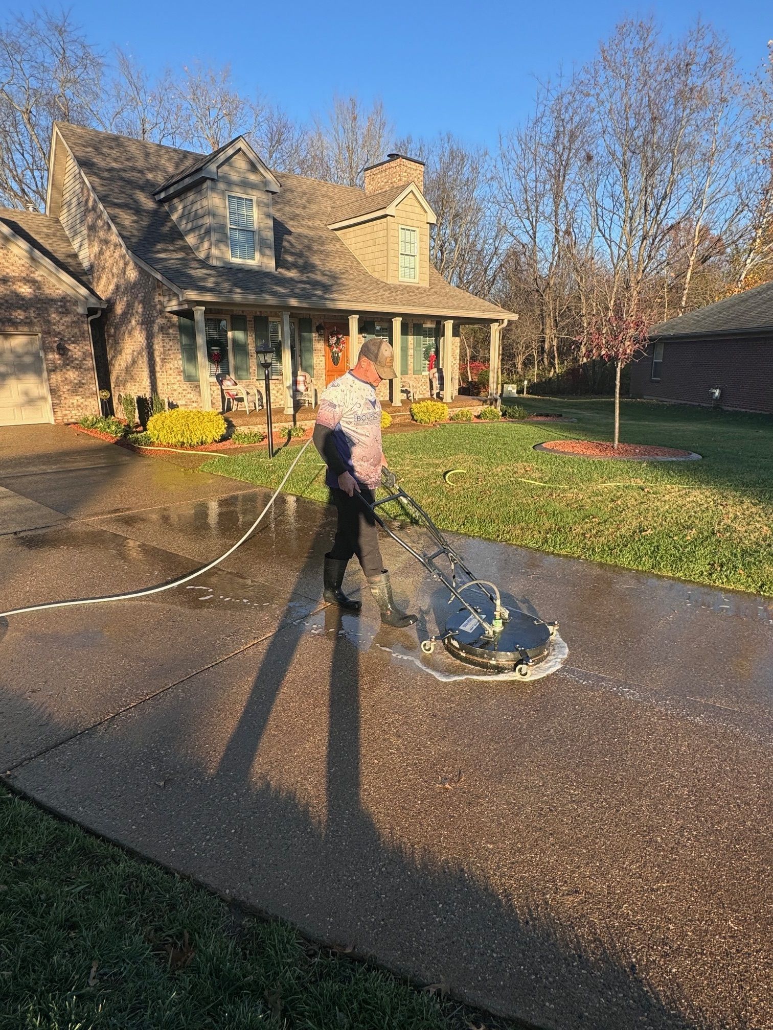 Person pressure washing a concrete driveway in front of a house.