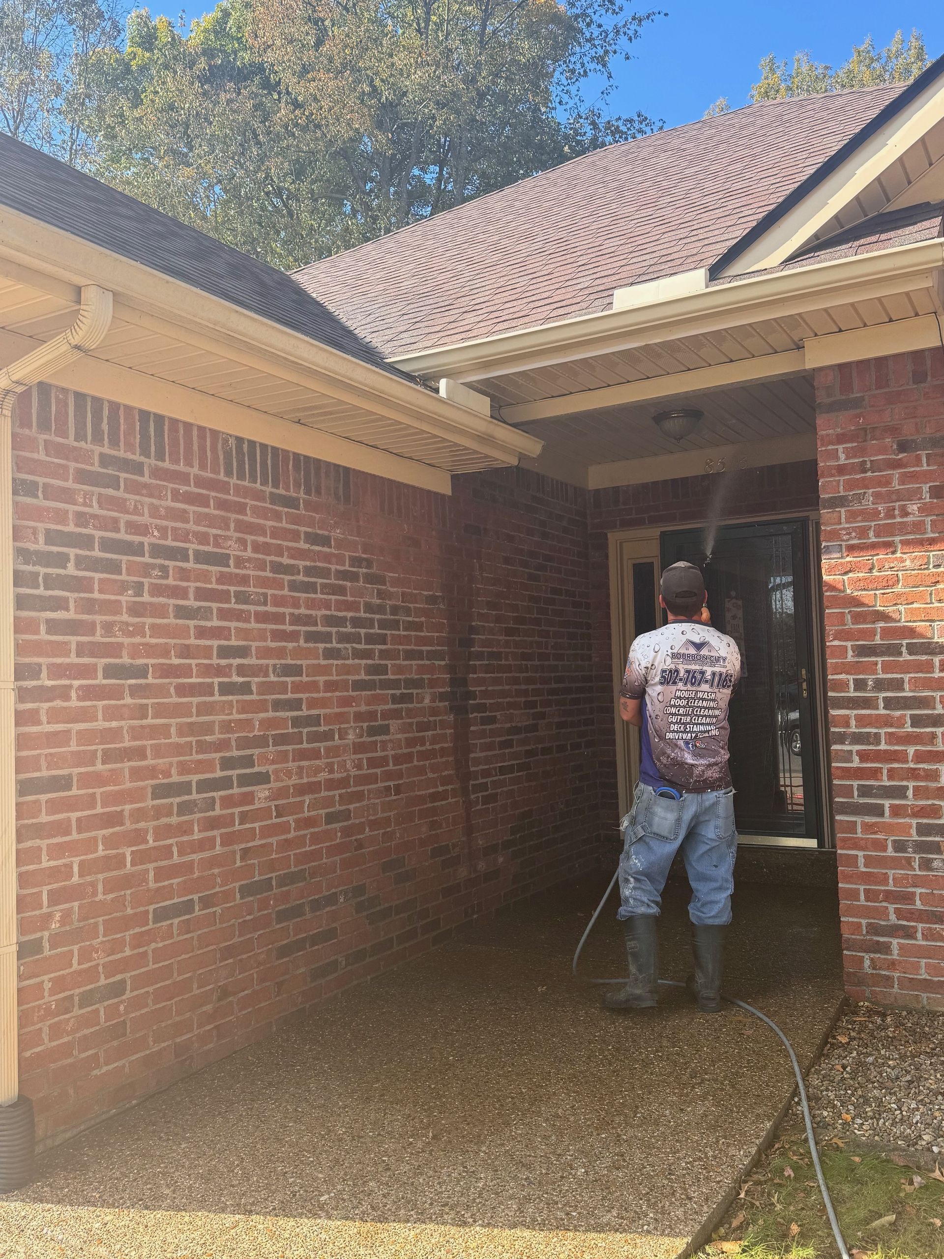 A Man Is Cleaning the Side of A Brick House with A Pressure Washer.