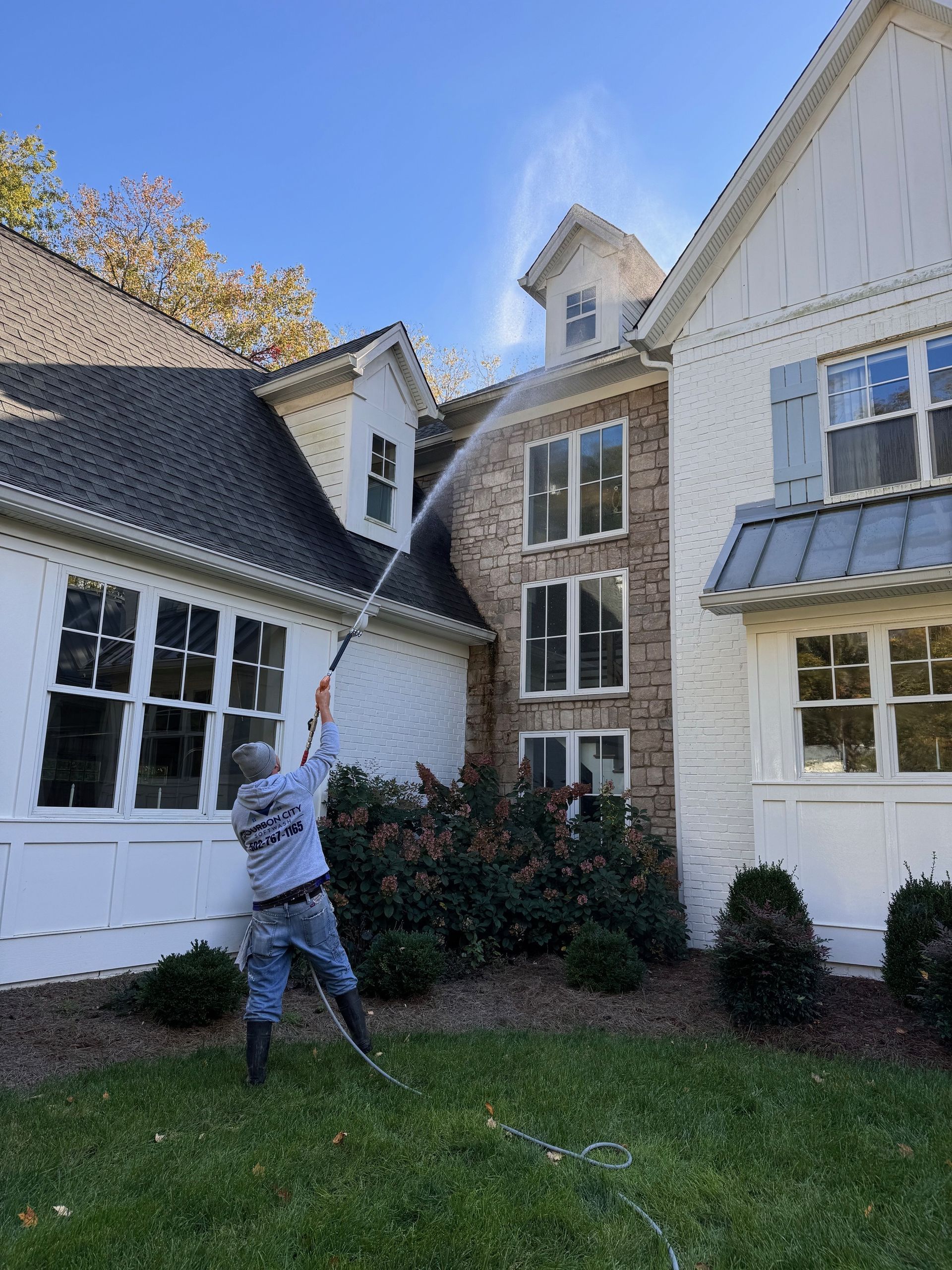 Man power washing the exterior of a two-story house with brick and white siding.