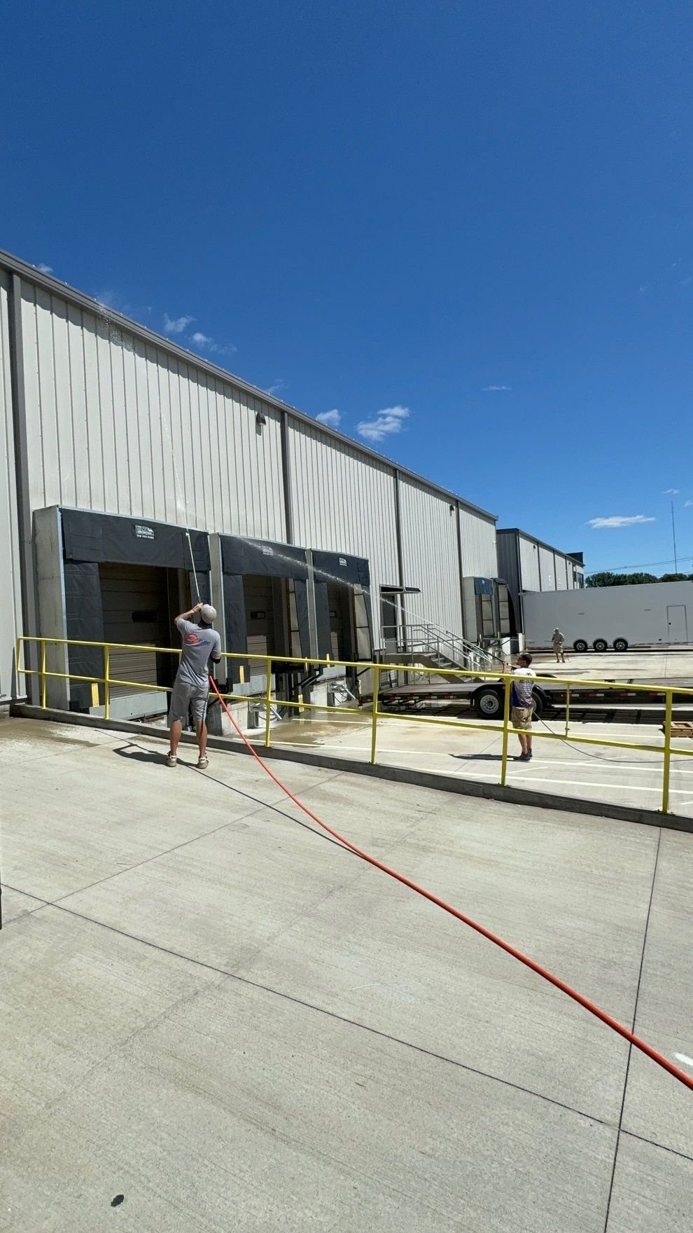 Person spraying water at loading docks on a bright day. Industrial building, blue sky.