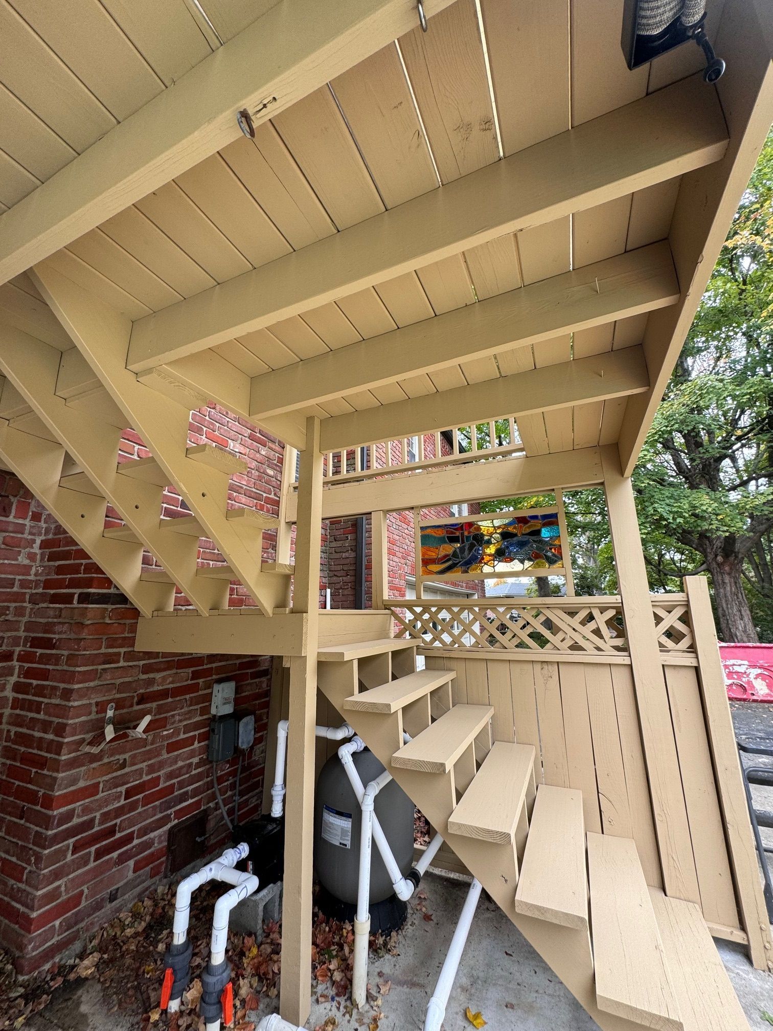 Wooden deck and stairs painted beige over a brick wall; pool equipment below.