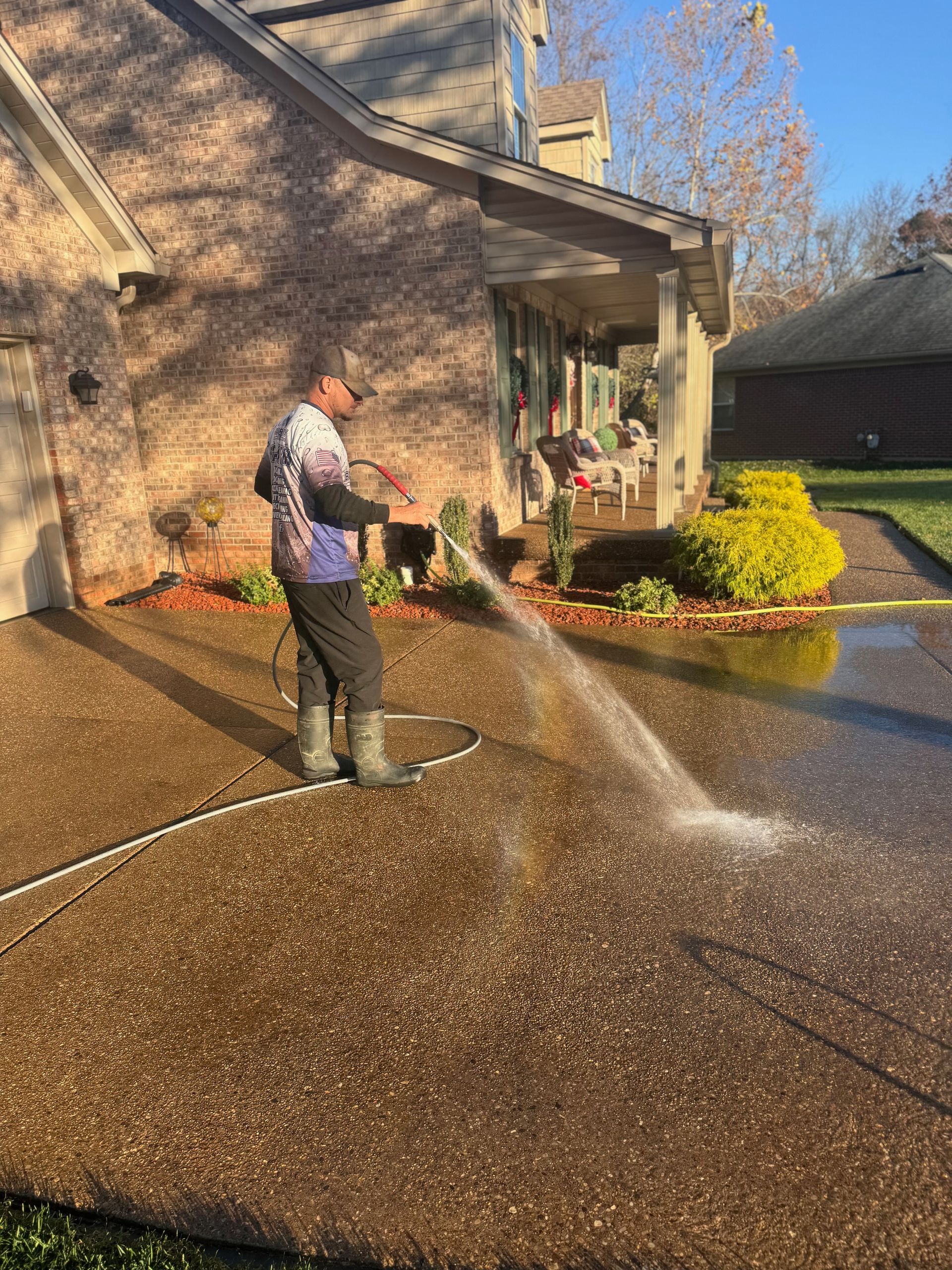 Person pressure washing a concrete driveway in front of a house.