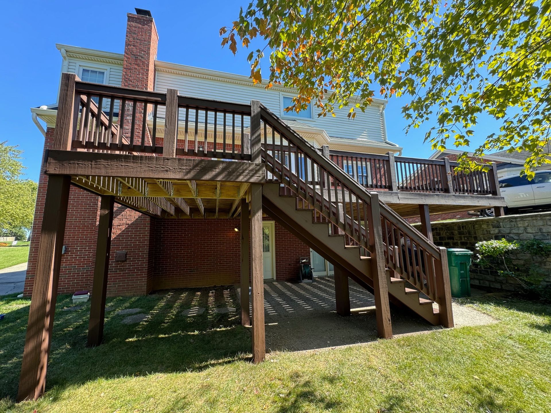 Brown wooden deck with stairs attached to a brick house, sitting on a grassy yard.