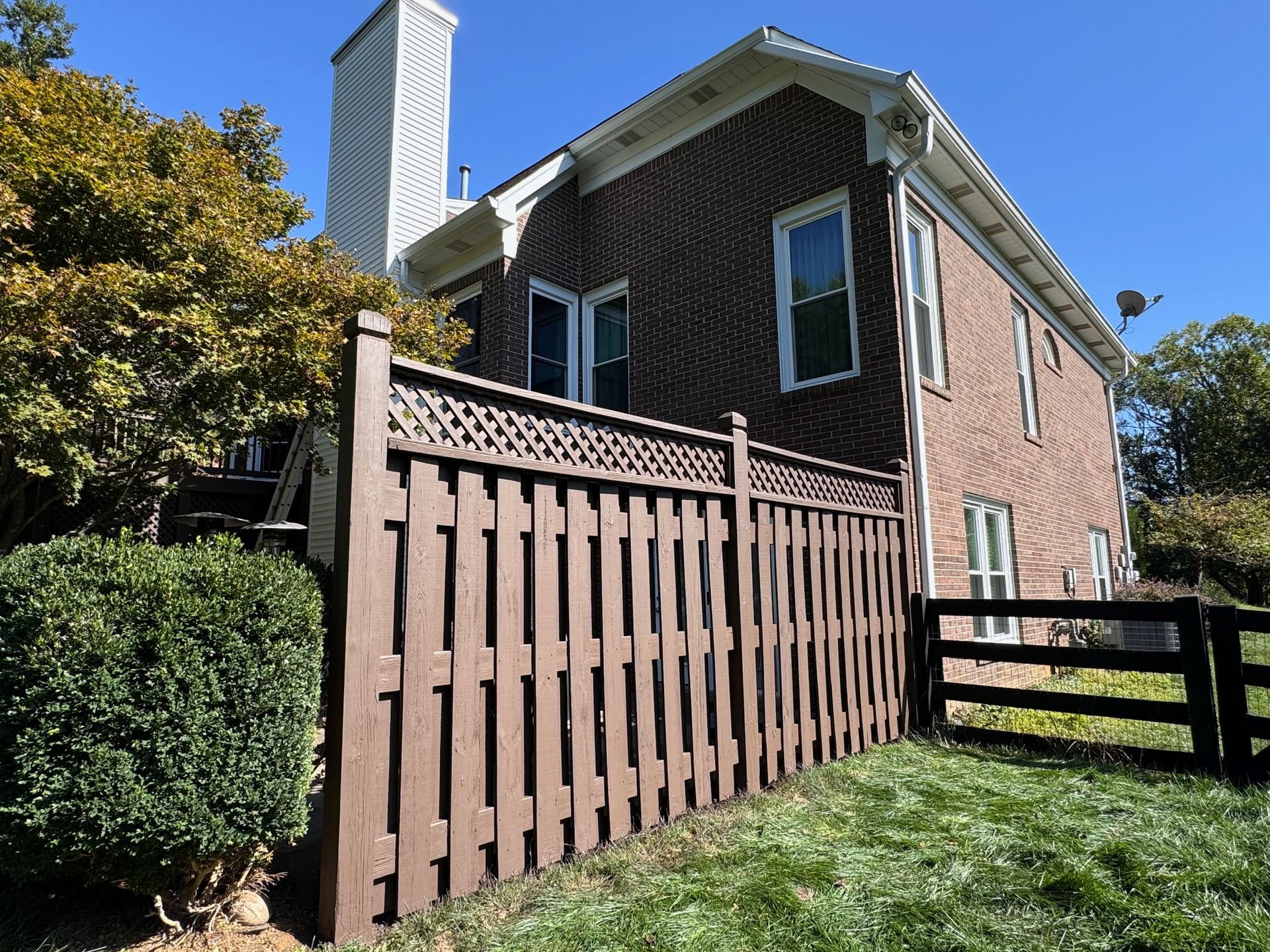 Brown fence along a brick house with a white chimney and green lawn.