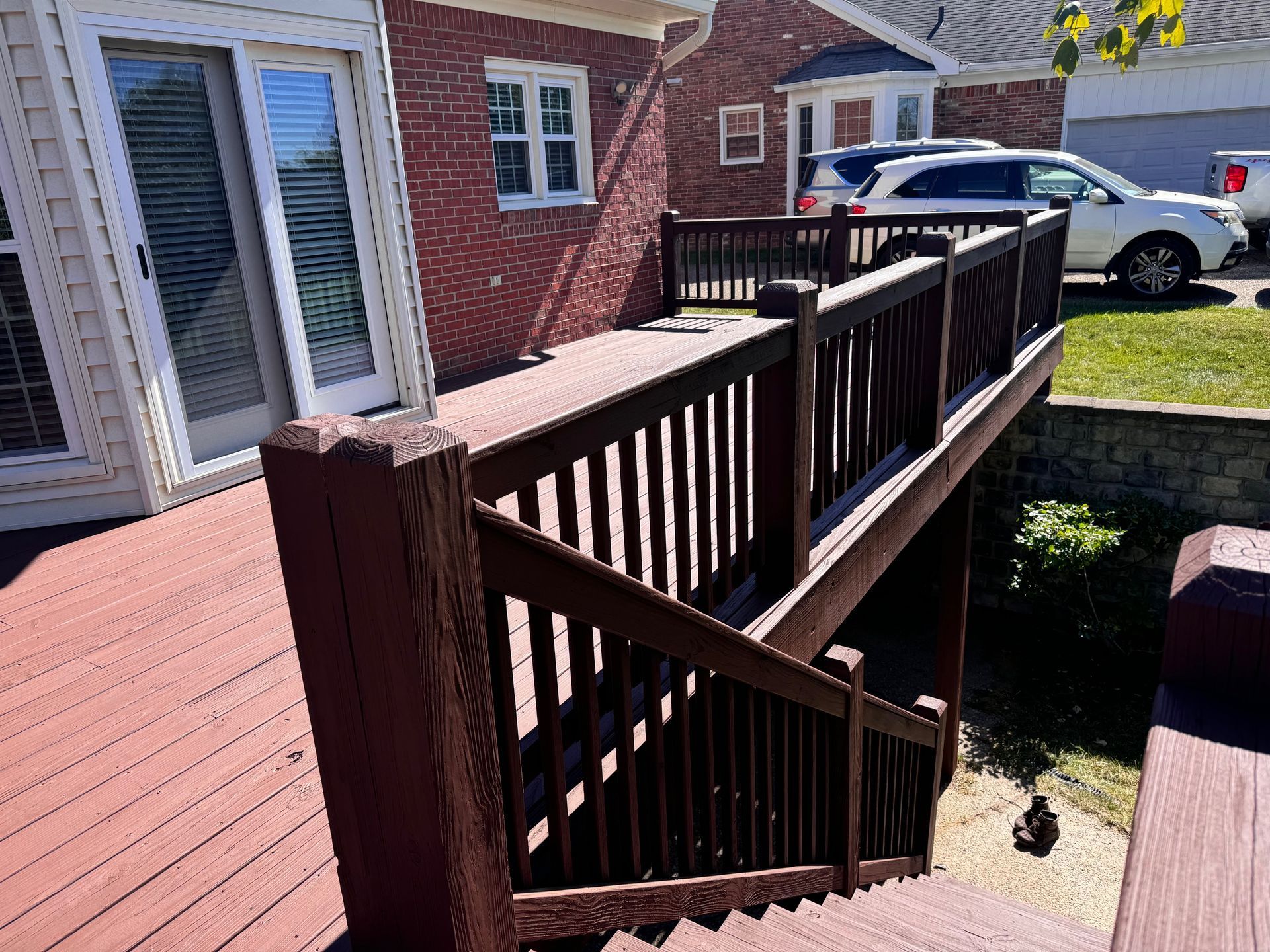 A wooden deck with brown railings and stairs leads to a backyard with a red brick house.