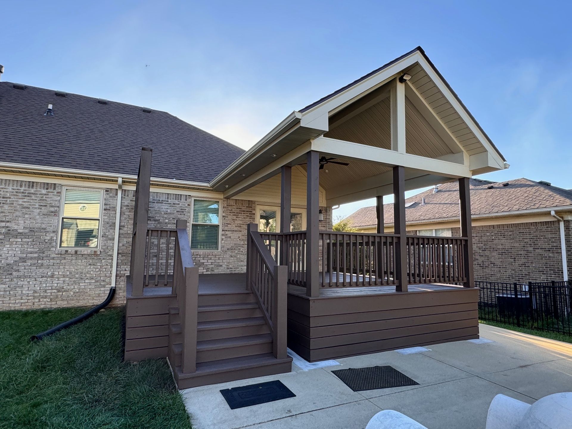 Brown deck with stairs, covered porch, attached to a brick house. Sunny outdoor setting.