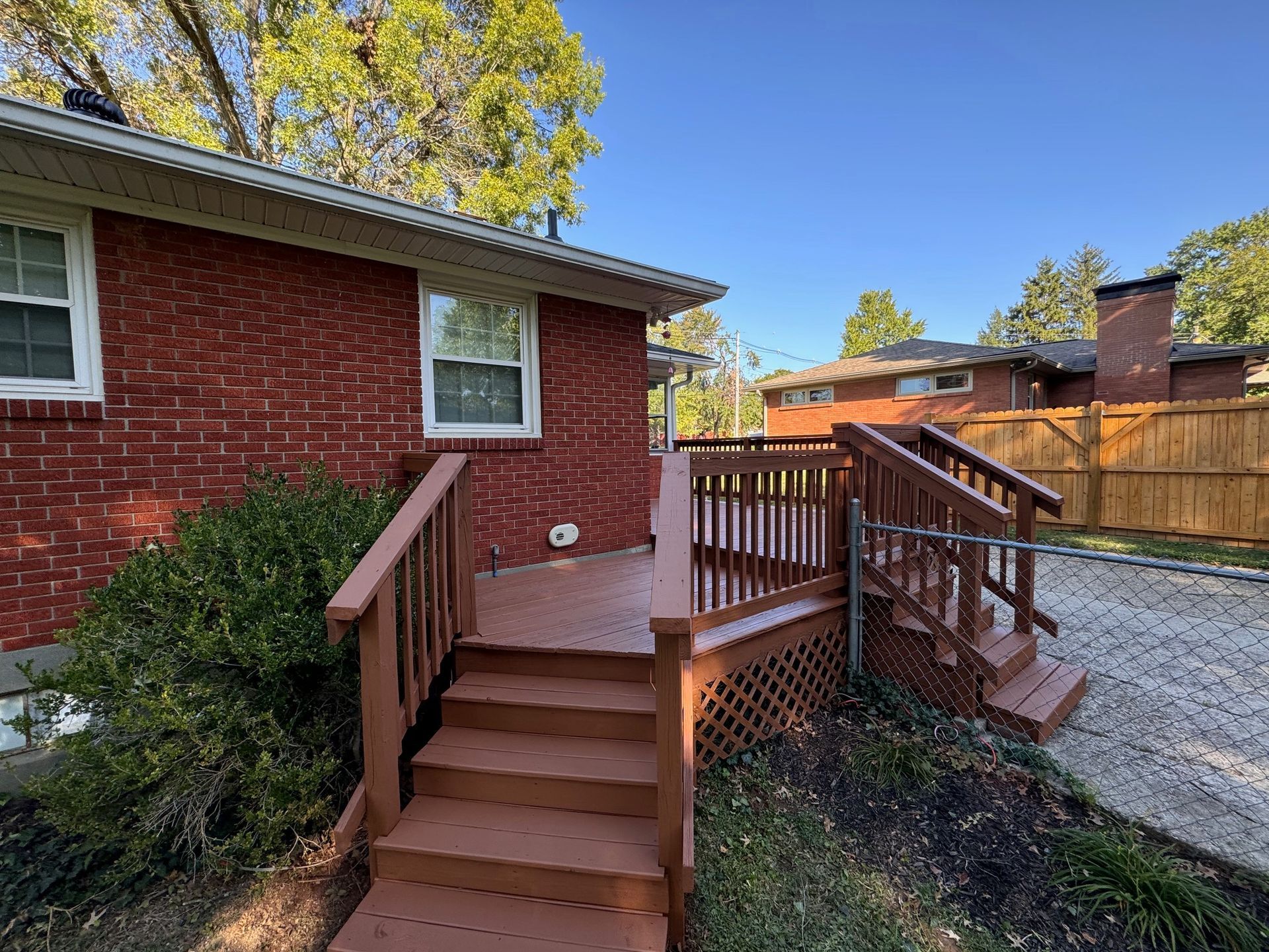 Red brick house with a brown wooden deck and stairs. Overcast sky.
