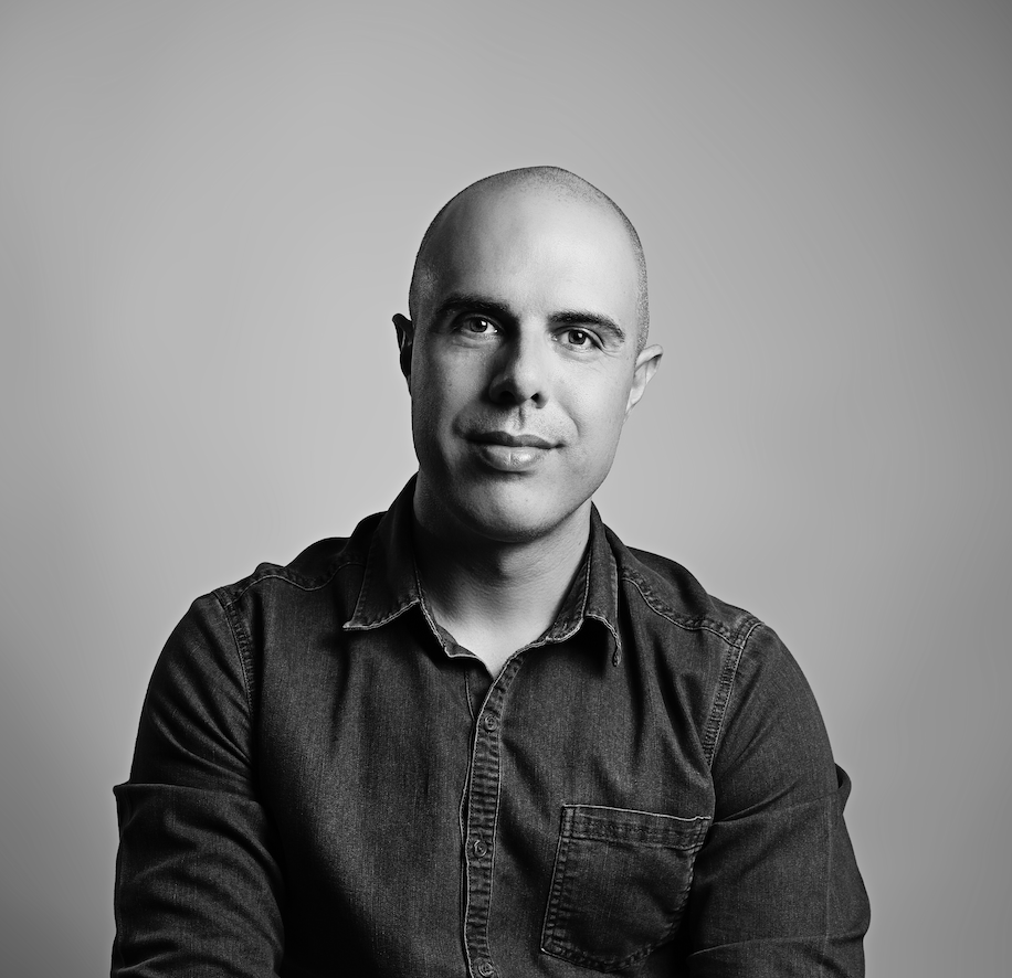 Um homem careca de camisa jeans sorri em uma foto em preto e branco