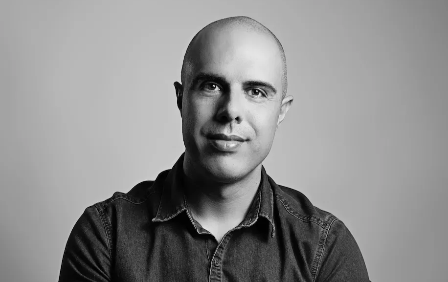 Black-and-white portrait of a bald person in a dark shirt, facing forward with a slight smile.