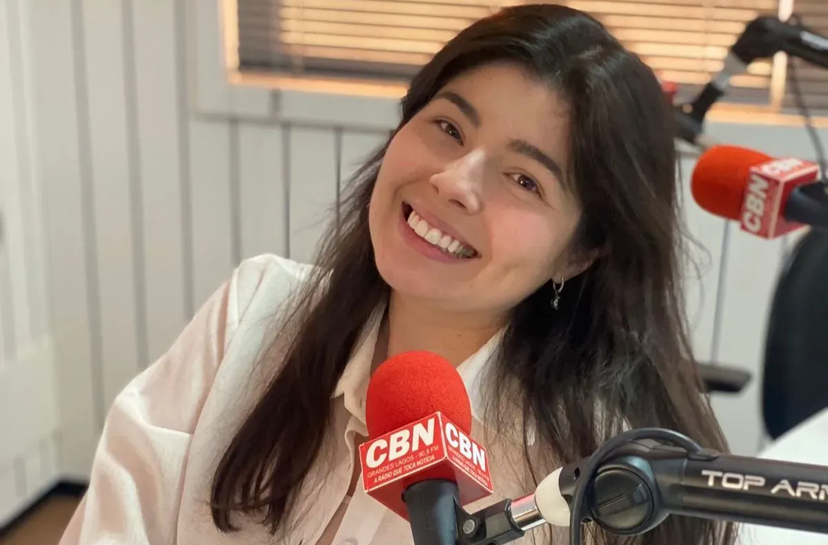 Mulher sorrindo, sentada em um estúdio de rádio com microfones da CBN.