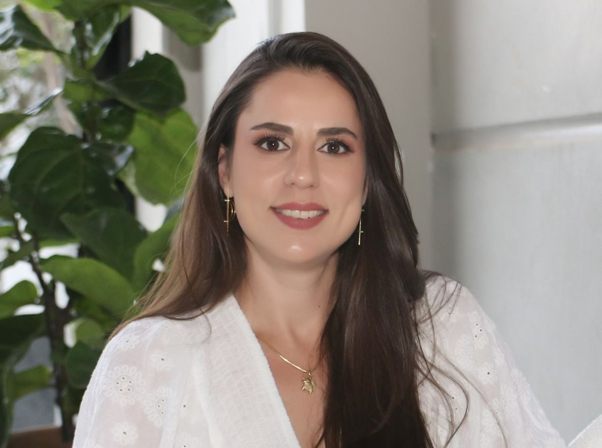Uma mulher vestindo uma camisa branca e um colar está sorrindo para a câmera.
