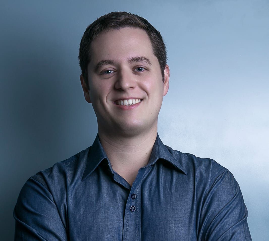 Um homem de camisa azul está sorrindo com os braços cruzados.