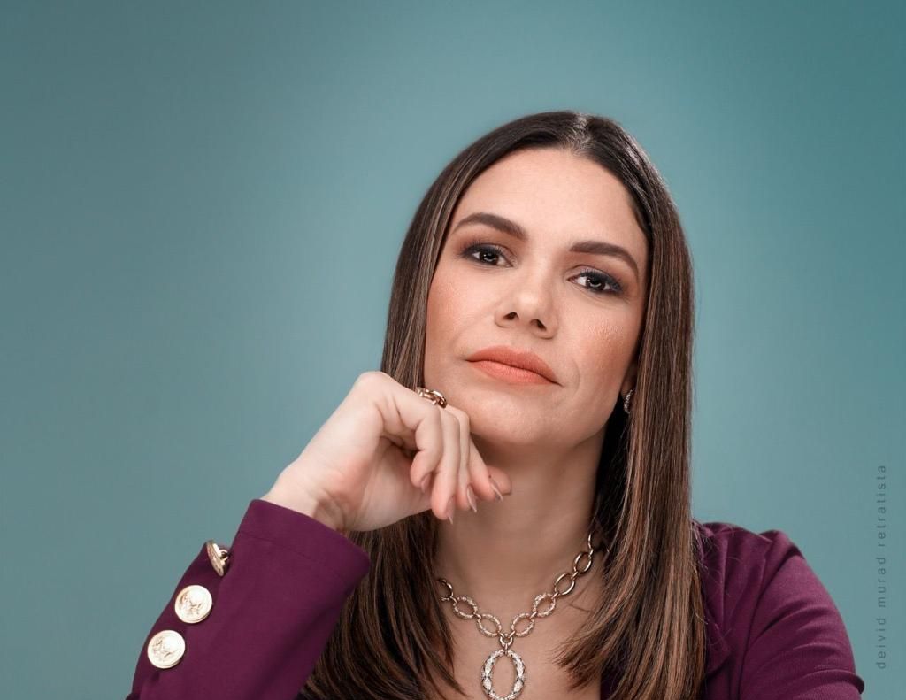 Uma mulher vestindo uma jaqueta roxa e um colar com a mão no queixo.