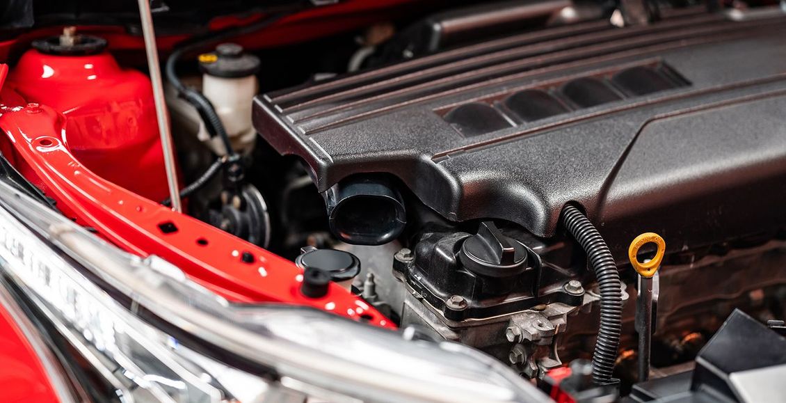 Red car engine bay with black engine cover and dipstick. | Stu's Collision Center
