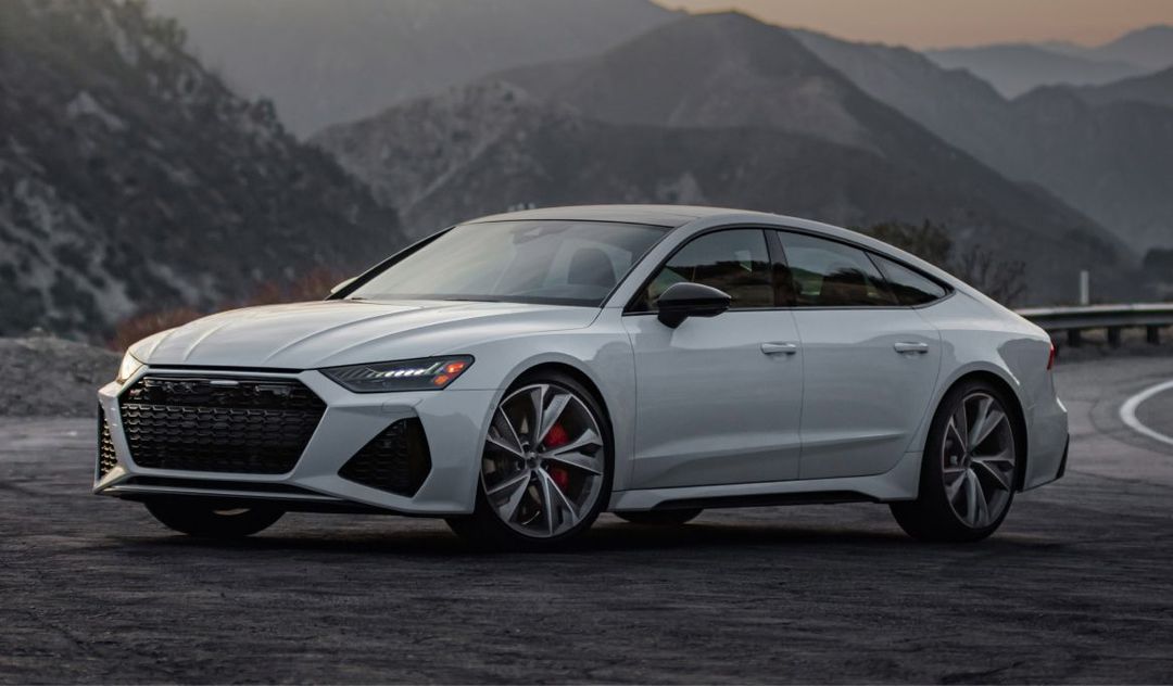 White Audi RS 7 on a winding road with mountains in the background. | Stu's Collision Center