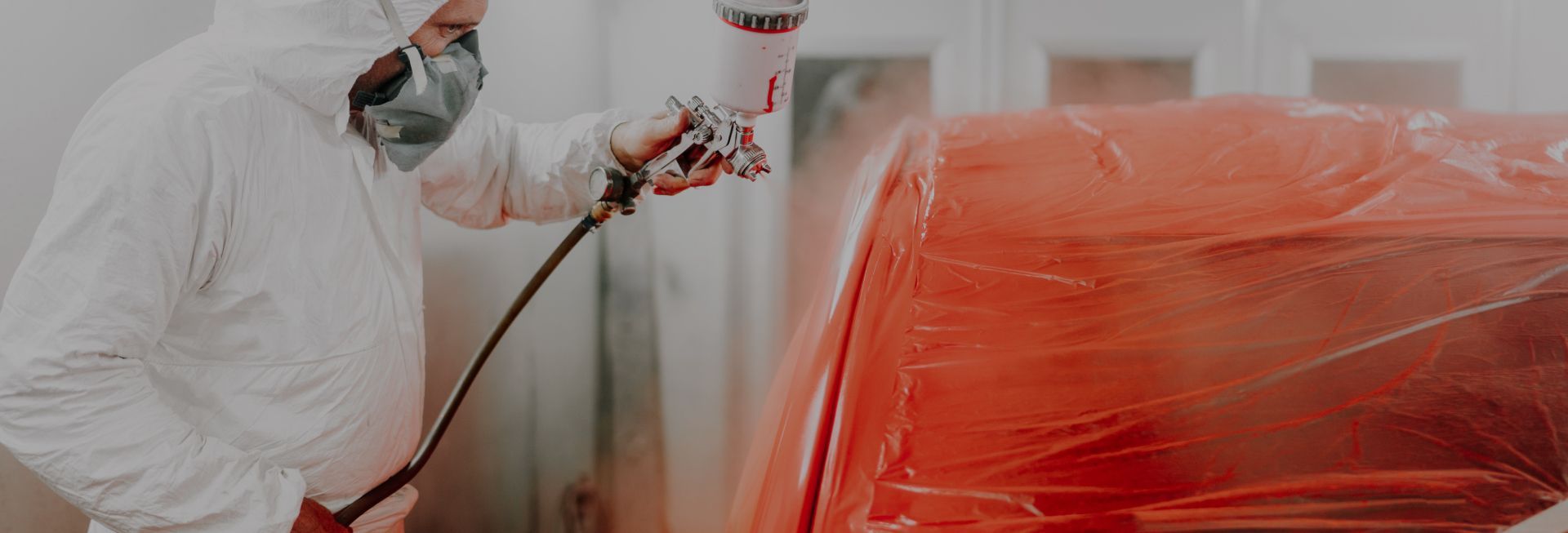 Person in white protective suit spraying red paint onto a car in a paint booth. | Stu's Collision Center
