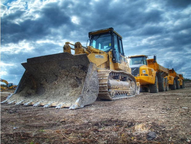 Yellow bulldozer and dump trucks on a construction site under a cloudy sky.