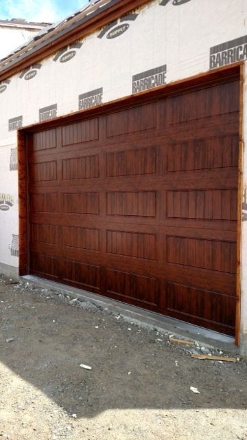Large brown wooden garage door set in a white stucco wall beside a dirt street.