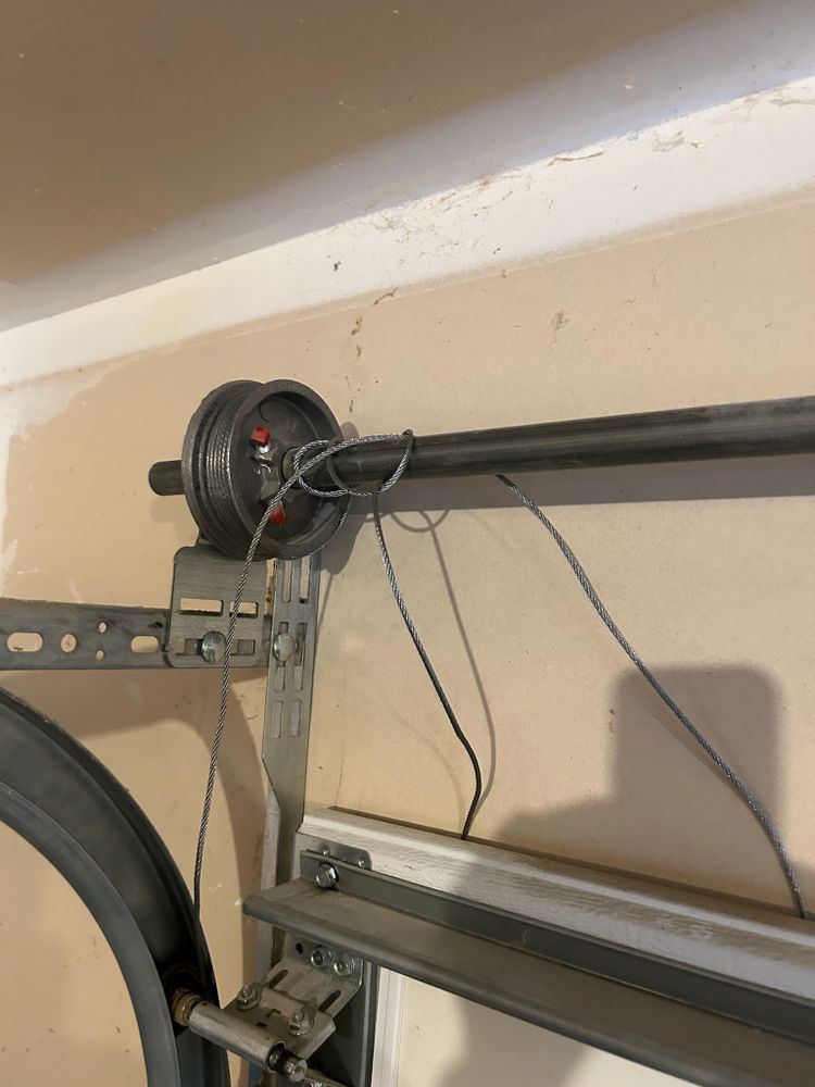 Garage door opener mechanism mounted near the ceiling with a black rail and hanging wires