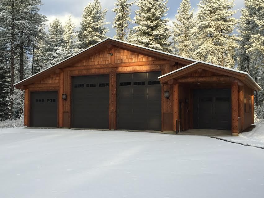 Snow-covered wooden garage with three dark doors in a winter forest setting