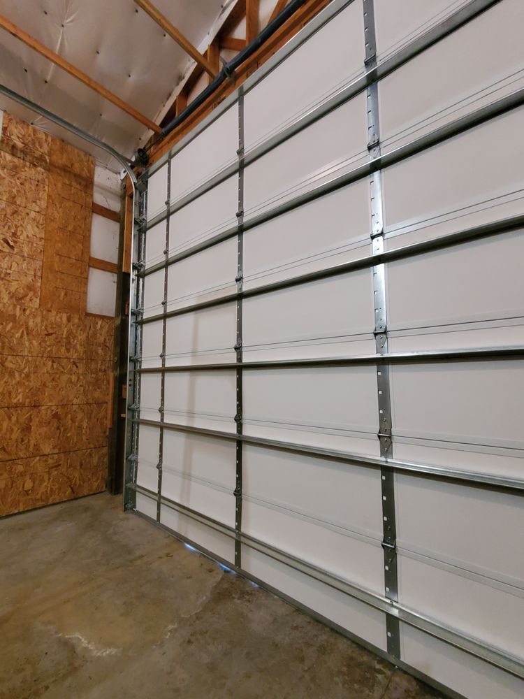 Interior of a garage with a closed white sectional door and concrete floor, beside an unfinished wood wall