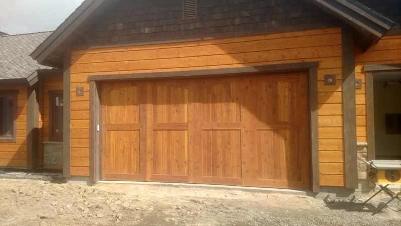 Wooden two-car garage door on a rustic house exterior with stone and wood siding.