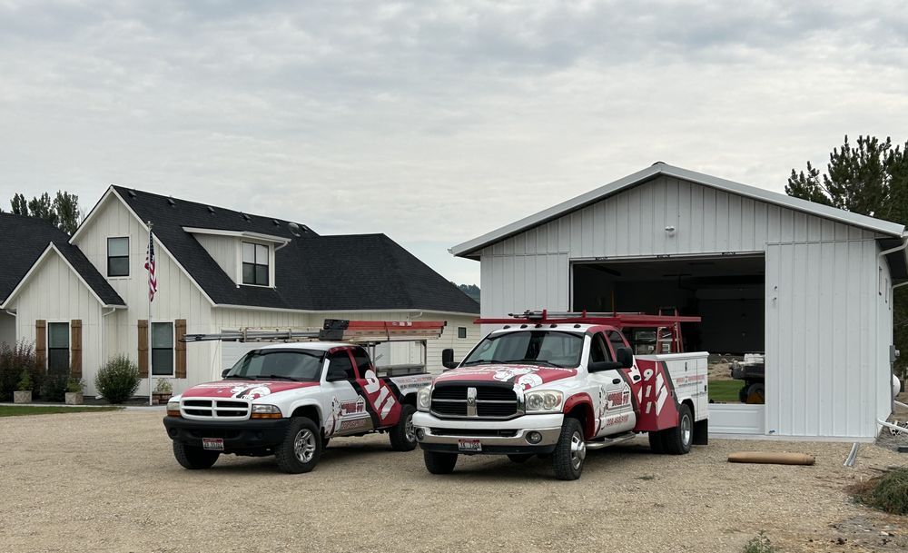 Two red-and-white emergency vehicles parked outside a house and large garage.
