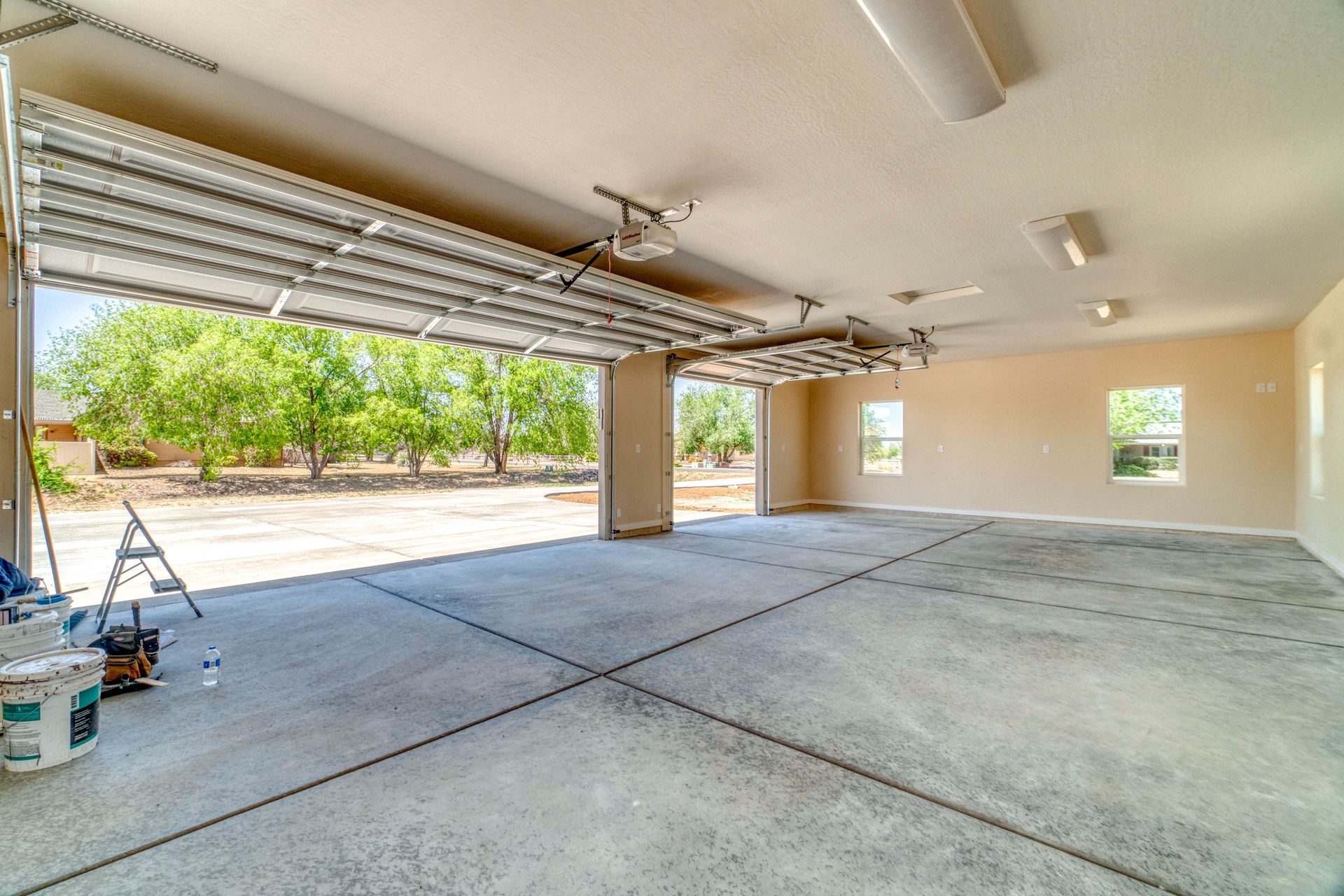 Empty two-car garage with open roll-up doors, concrete floor, and a small ladder near the left wall.