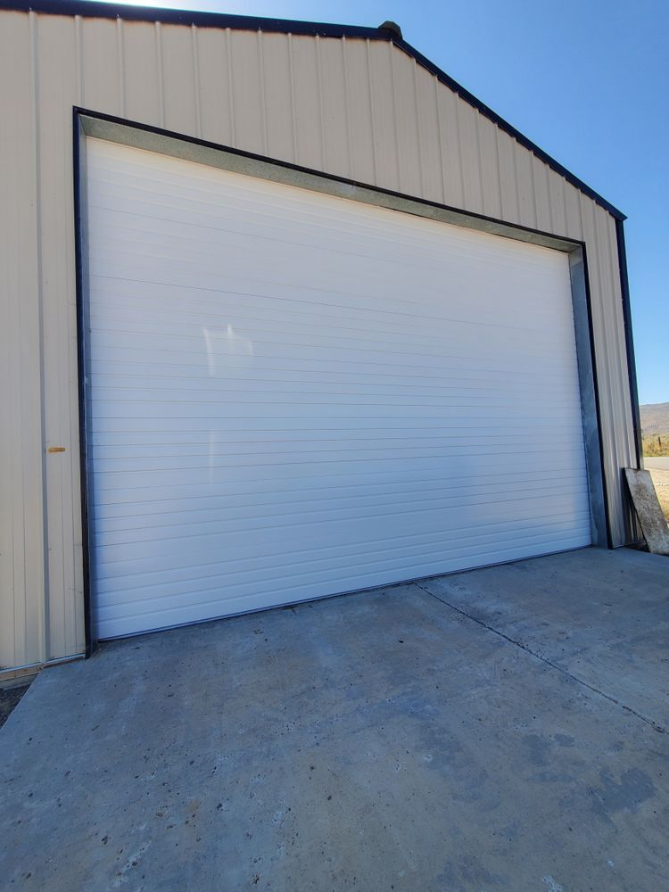 Large white roll-up garage door on a beige metal building, viewed from a concrete driveway.