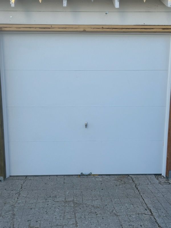 Closed white garage door on a driveway with gray brick paving.