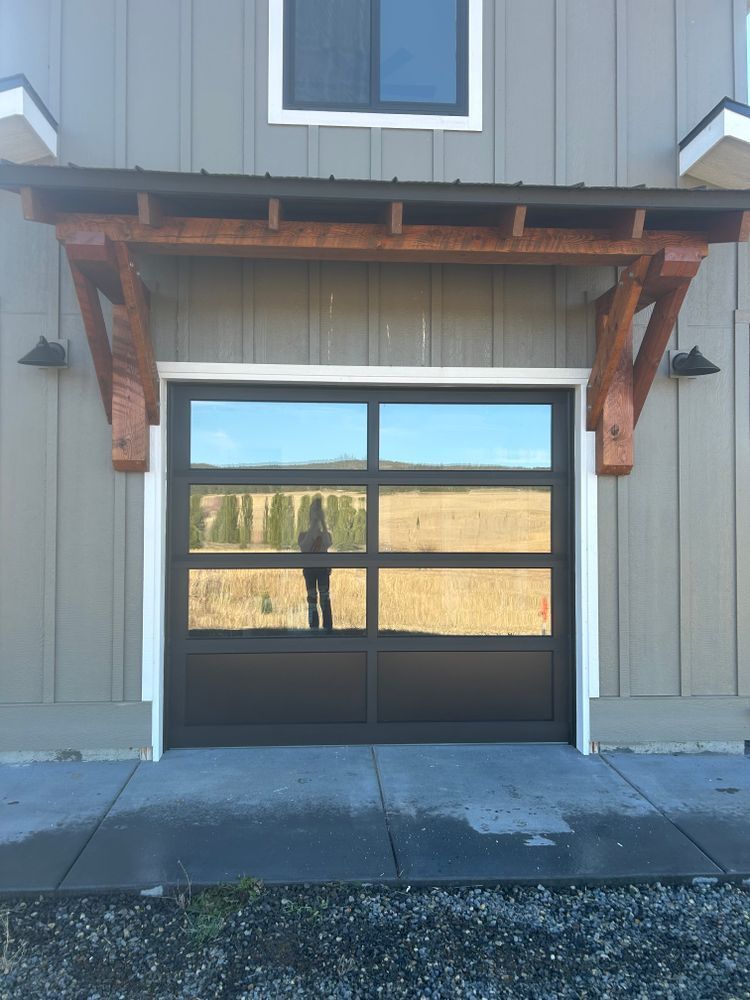 Gray building facade with a black-framed glass garage door and wood awning.