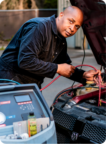 Mechanic using jumper cables to service a car battery under the open hood | EZT Auto and Transmissions