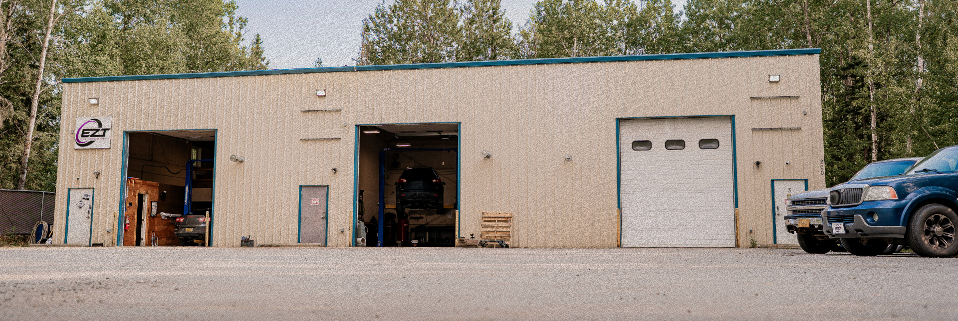 Single-story beige industrial building with garage doors, a bike by the entrance, and a blue truck parked | EZT Auto and Transmissionsoutside