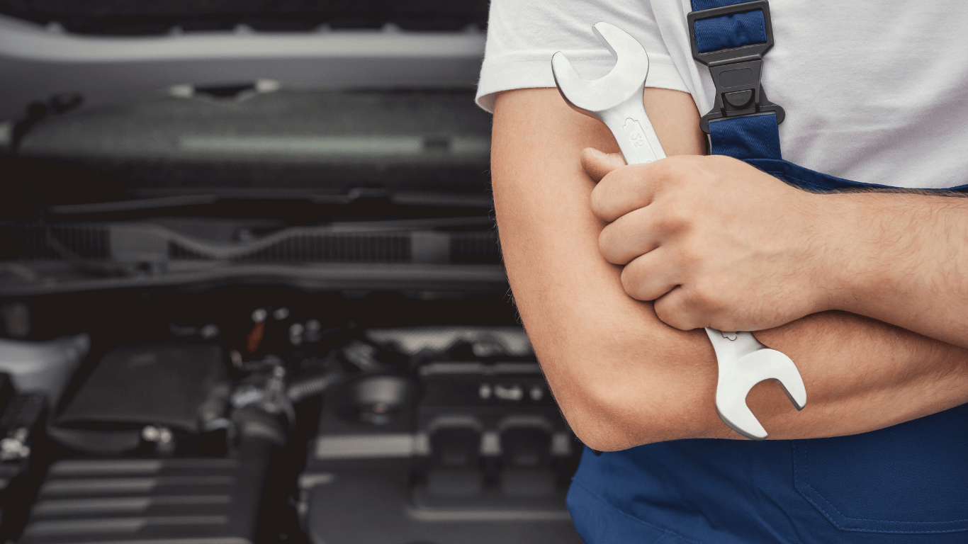 a mechanic holding a wrench in front of a car
