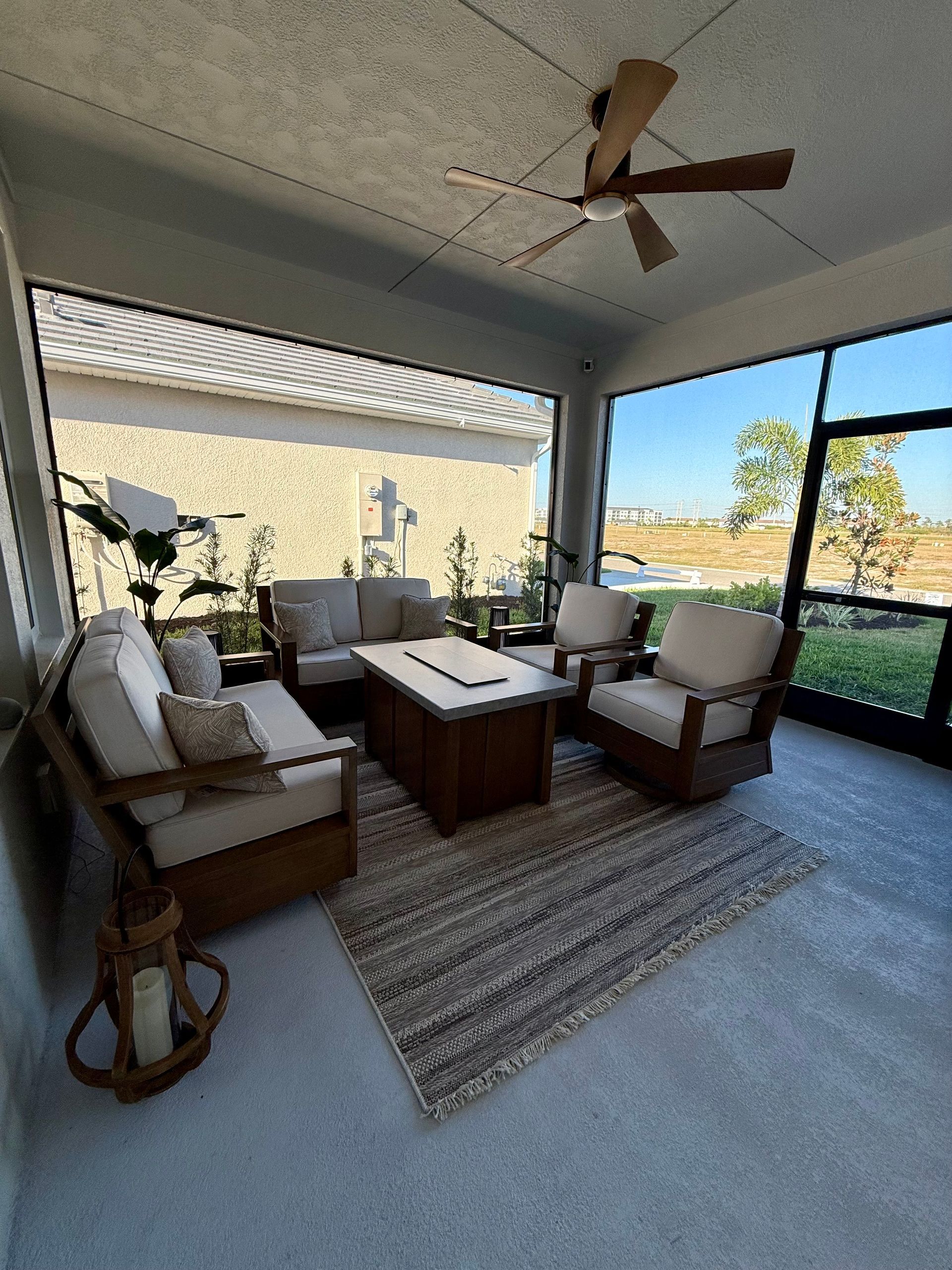 Cozy outdoor living space with beige furniture, a rug, and a ceiling fan, overlooking a sunny landscape.